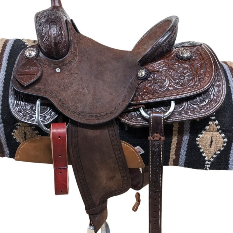 This Scott Thomas is stunning! The dark leather is paired alongside a leather pencil roll cantle and hard seat. The rough-out seat jockey and fenders provides the perfect grip. The combination diamond border and floral tooling makes this functional saddle also beautiful. Comes with a rear cinch and saddle strings. Features: Weight: Approx. 33 lbs Gullet: 7" mid-concho to mid concho Finished Seat Size: 14.5"