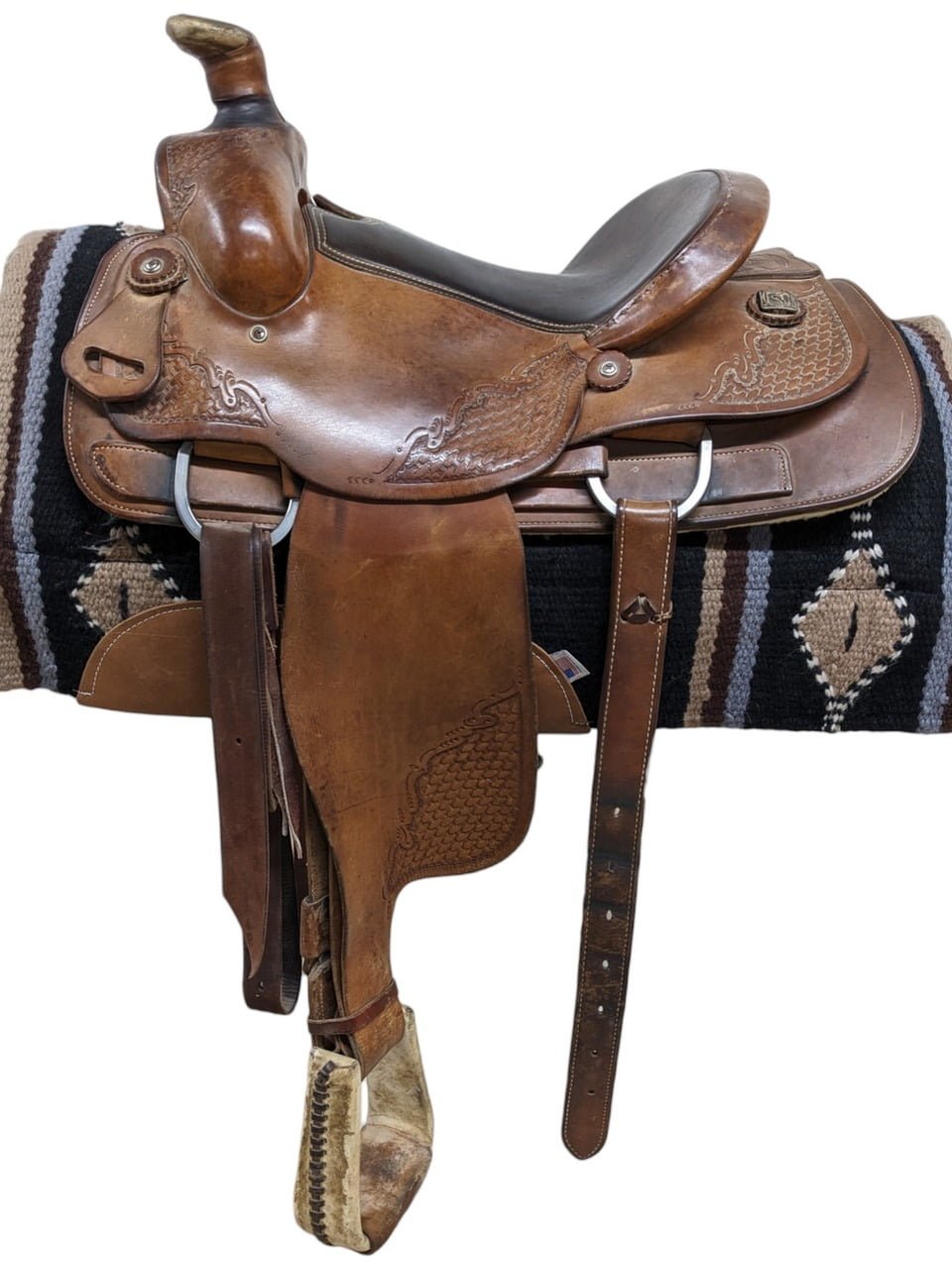 Consider this used McCall roper. This saddle features a padded seat for comfort and smooth leather. The saddle is accented by basket stamp and filigree tooling. Comes with a rear cinch.  Features: Weight: Approx. 48 lbs Gullet: 6.75" mid-concho to mid concho Finished Seat Size: 14" Skirt Length: 27" Tree Size: 14.5"